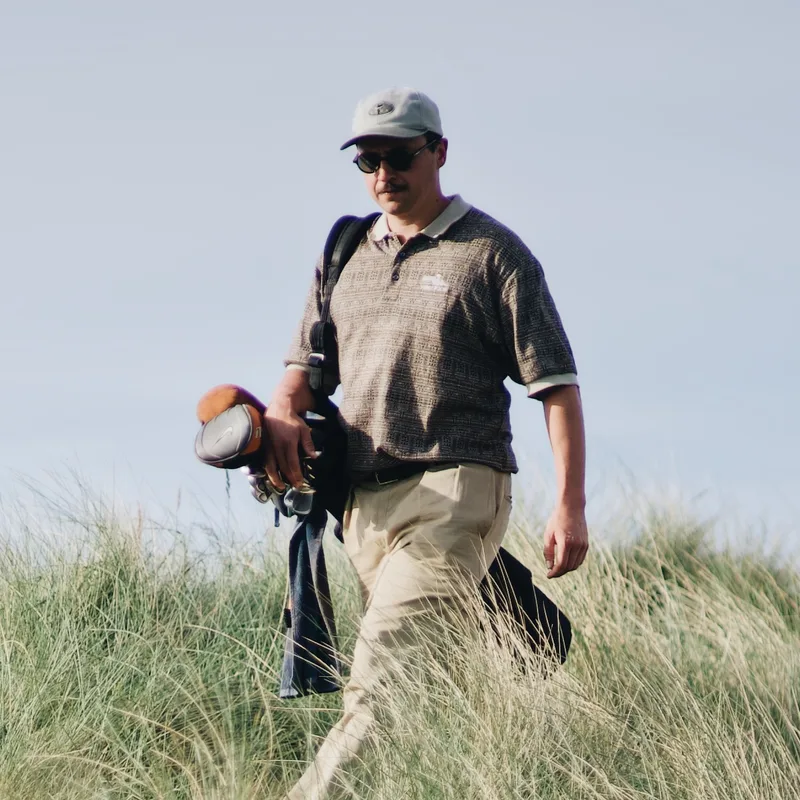 Ted, Strategy & Systems at Studio Nude, carrying his golf bag through the dunes